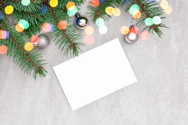 White sheet of paper on a gray background with a sprig of fir, festive balls and bokeh lights.