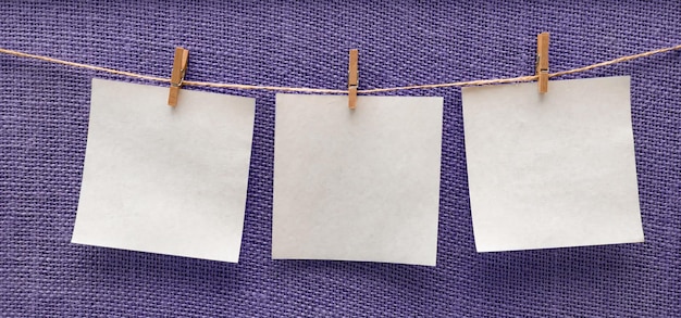 white sheets of paper hanging isolated on a violet beige board on clothespins free space mockup