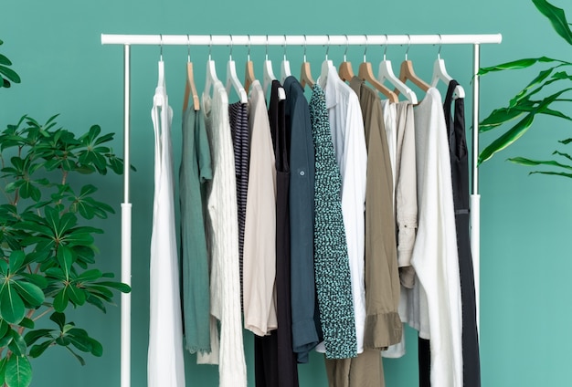 White shelf with a lot of clothes on the green background with green big plant.