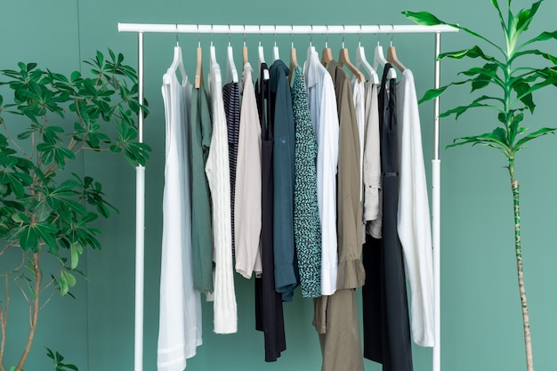 White shelf with a lot of clothes on the green background with green big plant.