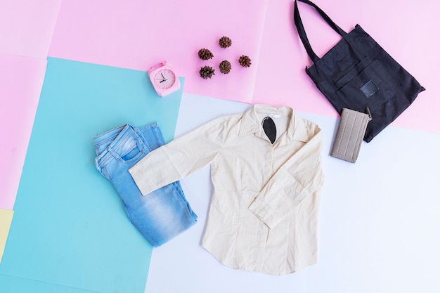 White shirt, blue jeans, brown purse and black bag on multi pastel color background