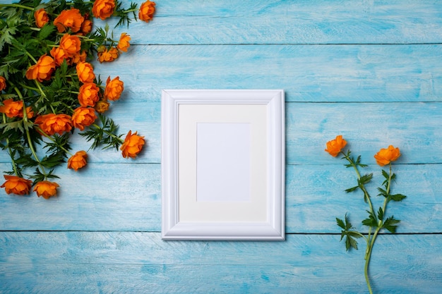 White small frame mockup with globeflowers bouquet on the blue wooden table. Empty frame mock up for presentation artwork. Template framing for modern art.