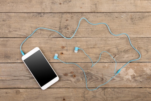 White smartphone with headphones on the old wooden board