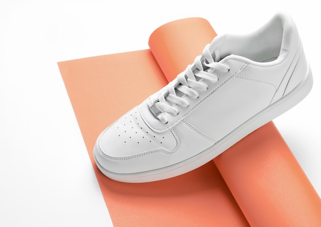 White sneaker on rolled-up roll of orange paper on a white background. Minimalism fashion