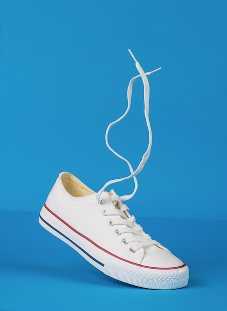 White sneakers with red stripes with floating laces on a blue background