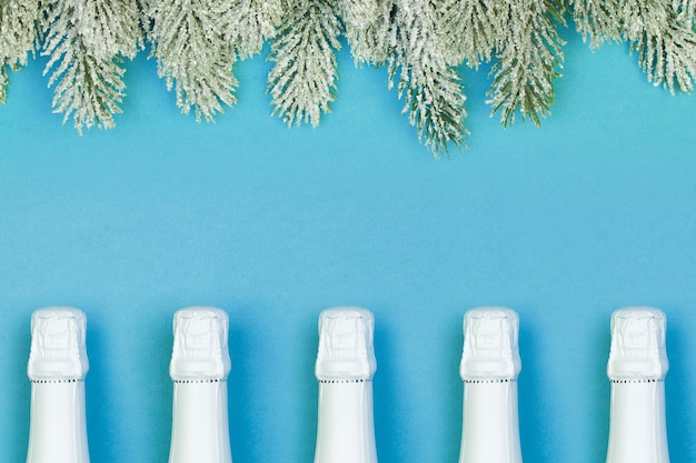 White Sparkling wine bottle and green Xmas tree branch on blue background Christmas concept