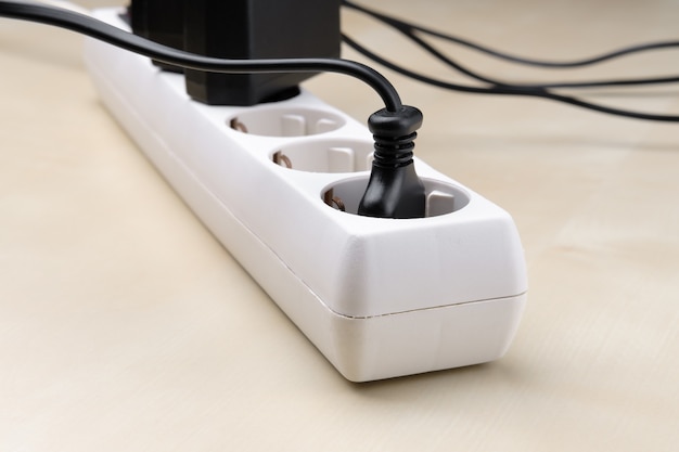 A white splitter socket with plugs from different devices included in it lies on the light surface of the diagonal.