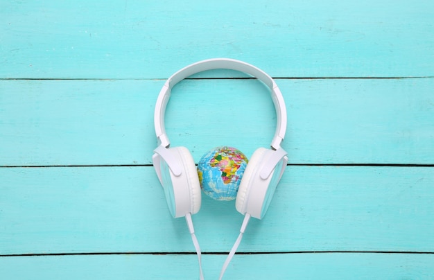 White stereo headphones with globe on blue wooden background World Music Day Top view