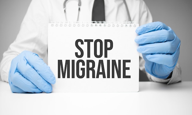 White sticker with text Stop Migraine in doctor's hands with a stethoscope