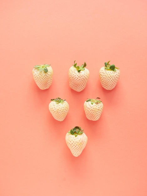 white strawberries arranged in a row forming a triangle on a pink background top view with copy spa