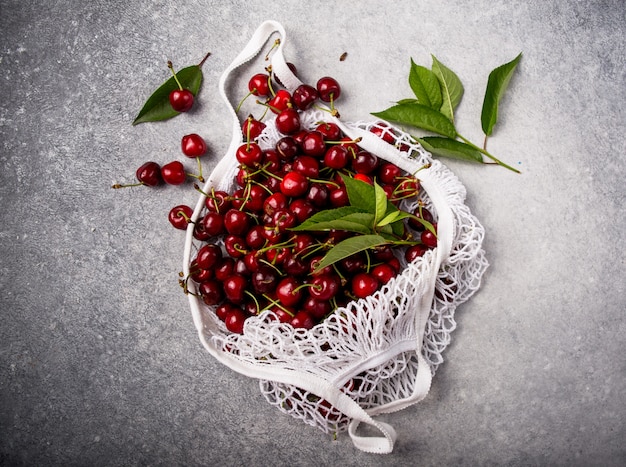 White string bag with fresh cherry  on a dark background. No plastic, only natural materials and products.