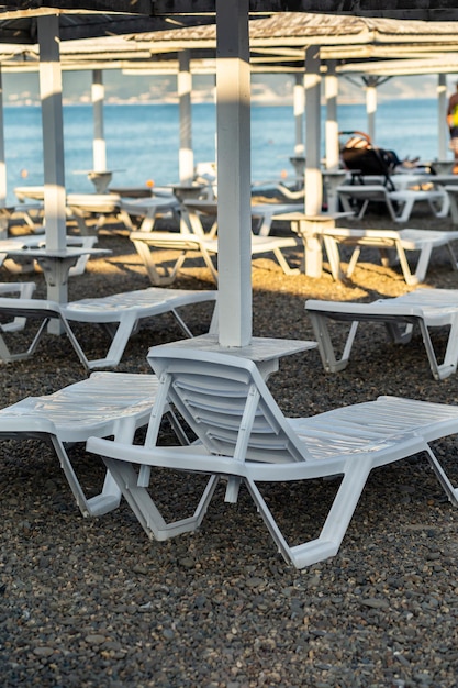 White sun loungers on a blurred pebble beach under an umbrella against the backdrop of the sea