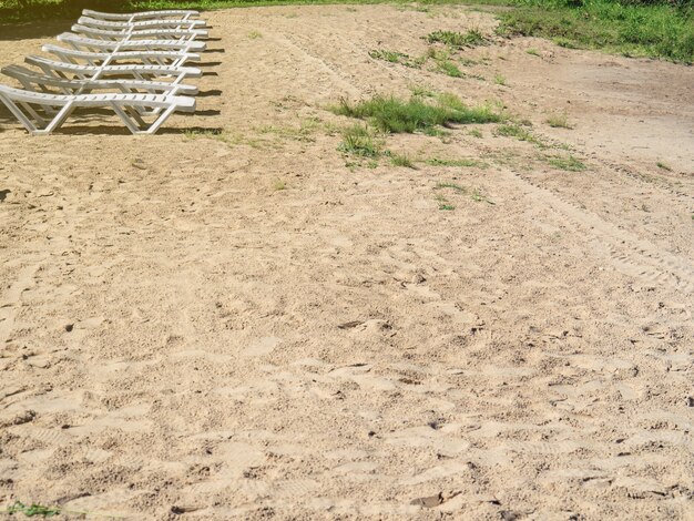 White sun loungers on the sandy shore of the reservoir summer vacation. Copy space.