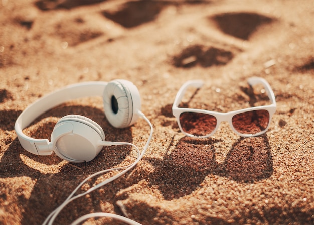 White sunglasses and headphones on sand