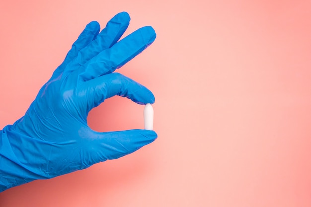 White suppository for anal or vaginal use in hand of a doctor wearing gloves on a pink background. Medical candles for treatment of Candida, thrush, hemorrhoids, inflammation and fever. Copy space