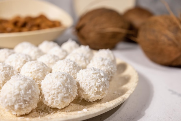 White sweet coconut candies in plate, coconuts and almond nuts on background, close up with selective focus. High quality photo