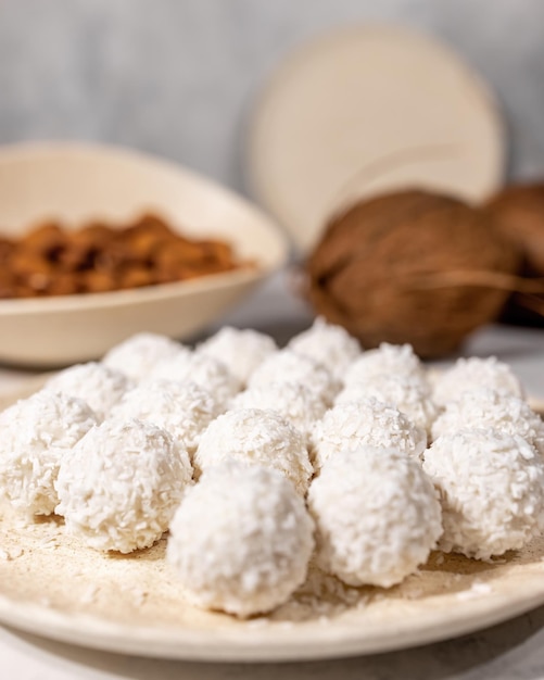 White sweet coconut candies in plate, coconuts and almond nuts on background, close up with selective focus, vertical. High quality photo