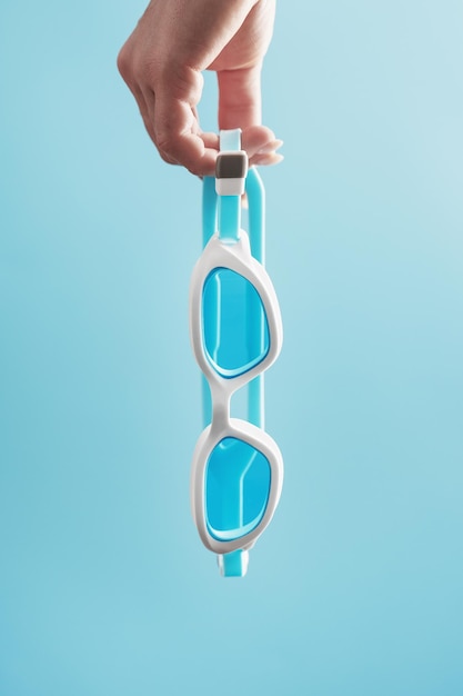 White swimming glasses in hand with a blue lens on a blue background