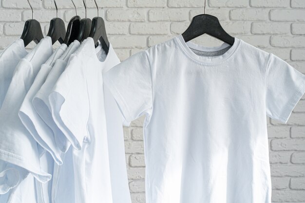 Photo white t-shirt hanging on hanger against brick wall, copy space