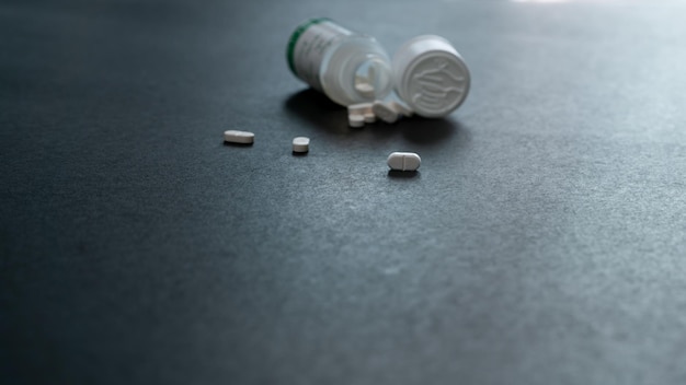 White tablets pills and blur plastic pill bottle on dark floor Prescription drugs Pharmaceutical