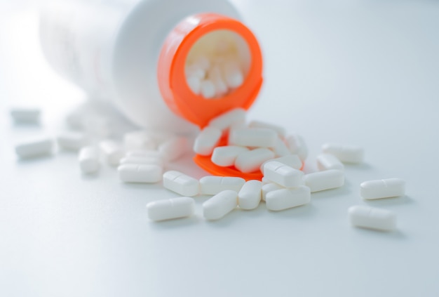 White tablets spilling out of plastic white bottle with a tablet