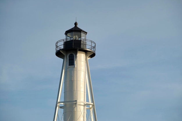 White tall lighthouse on sea shore against blue sky for commercial vessels navigation