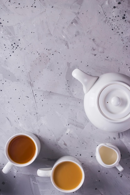 White teapot and white cups of tea or coffee on a gray table