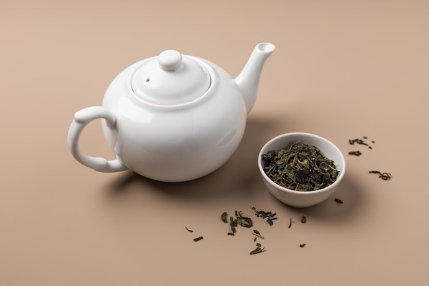 White teapot with a bowl of green tea on a beige background top view