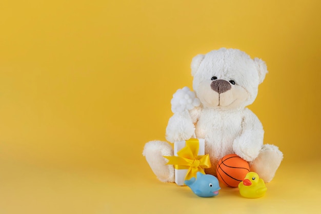 White teddy bear holding small white cloud and present with rubber ducky whale and orange ball