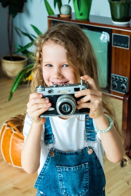 The white teen girl takes pictures on a retro camera and laughs hobby for kids and happy childhood