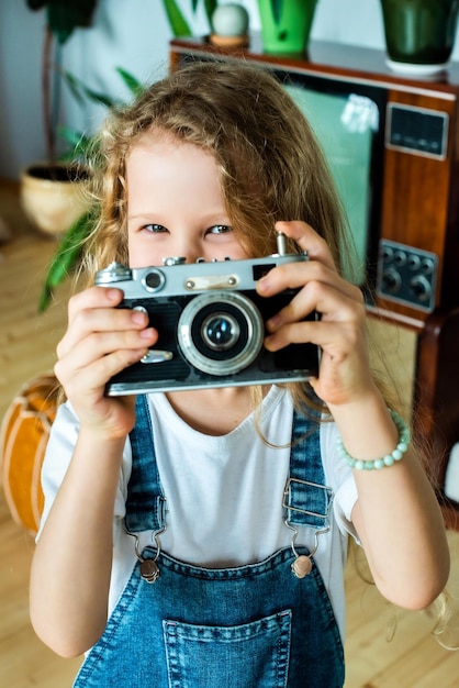 The white teen girl takes pictures on a retro camera and laughs hobby for kids and happy childhood