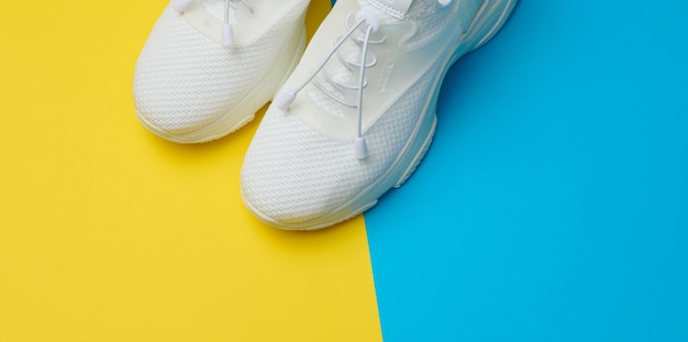 White textile sneakers on a blue yellow background top view