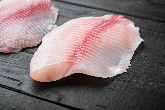 White tilapia fish fillet cuts on black wooden table