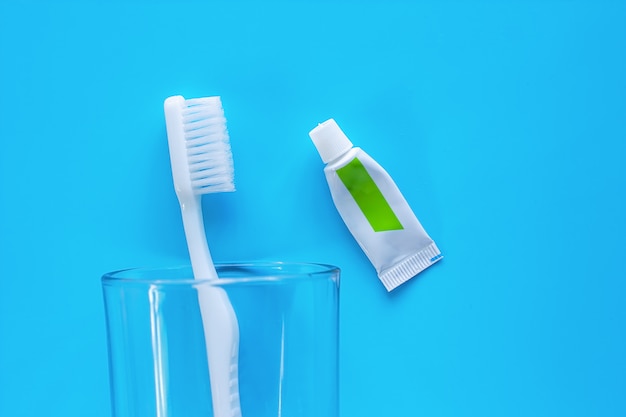 White toothbrush in the transparent glass with toothpaste used for cleaning the teeth on blue background