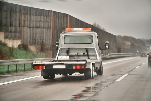 A white tow truck with orange lights on the back driving down the road.