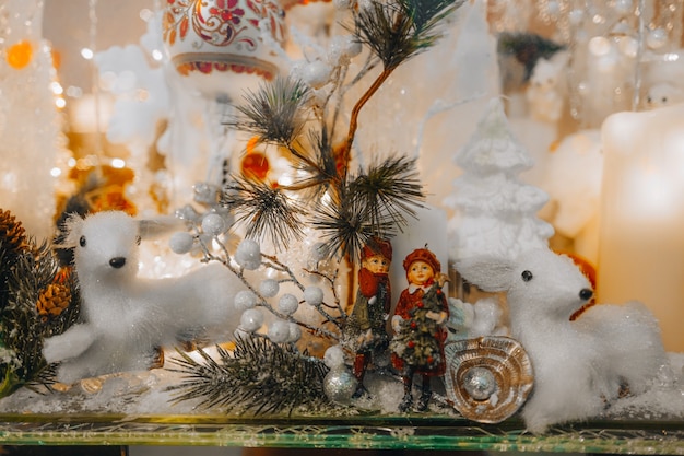 White toy fawns and Christmas tree branch with silver glitter on a festive storefront New Year