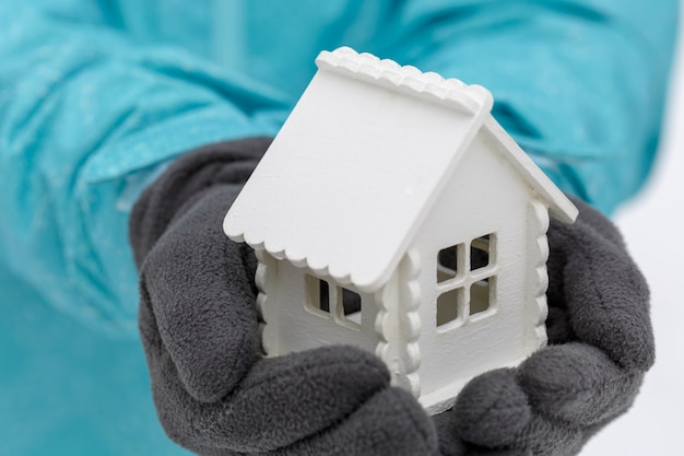 White toy house in the hands of a man wearing dark gloves