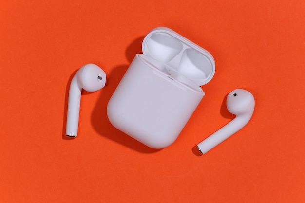 White true wireless bluetooth headphones or earbuds with charging case on orange bright background.