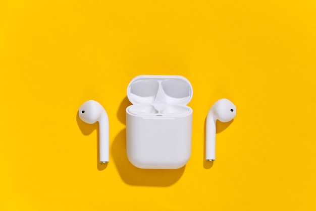 White true wireless bluetooth headphones or earbuds with charging case on yellow bright background.