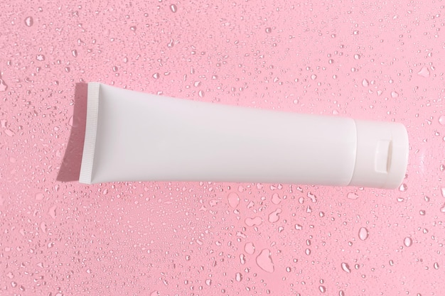 White tube of cosmetic cream In splashes of water On a pink background