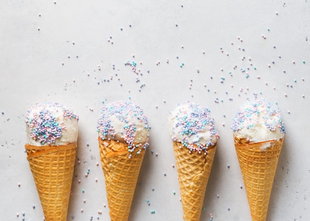 White vanilla ice cream scoop in waffle cone with sprinkles on light grey background