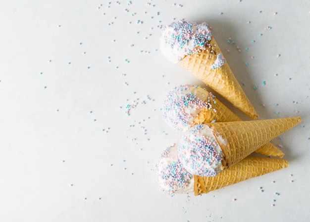 White vanilla ice cream scoop in waffle cone with sprinkles on light grey background