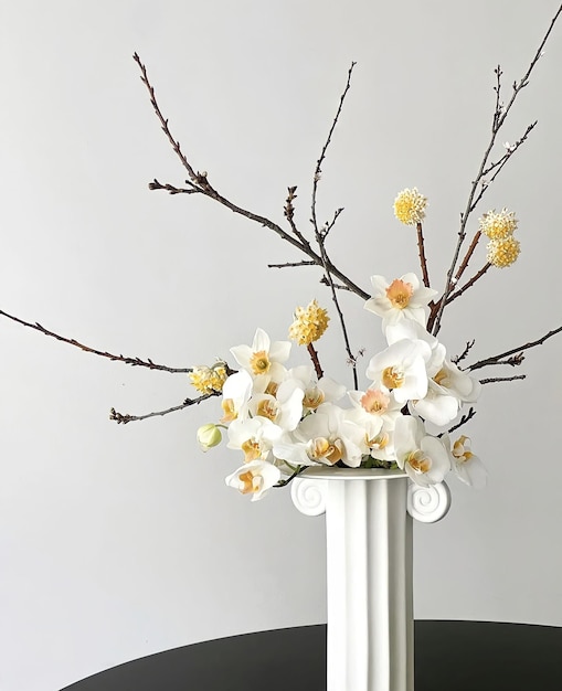 A white vase with a branch of a tree with white flowers in it.