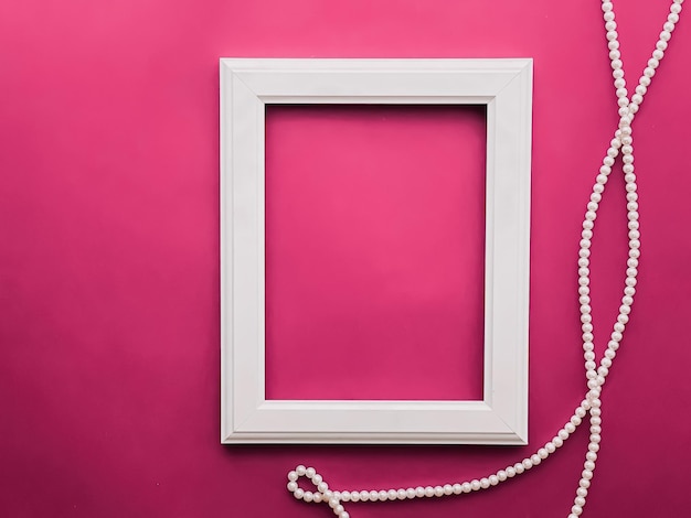 White vertical art frame and pearl jewellery on pink background as flatlay design artwork print or photo album