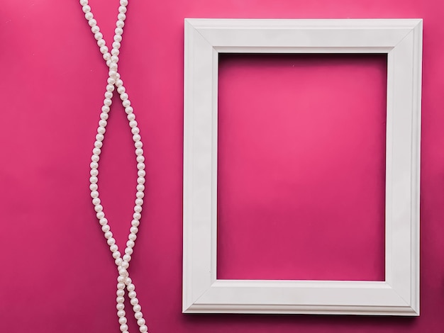 White vertical art frame and pearl jewellery on pink background as flatlay design artwork print or photo album