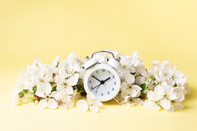 White vintage alarm clock in cherry flowers on yellow