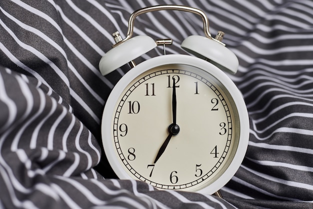 White vintage alarm clock on pillow in bed. Wale up and morning concept