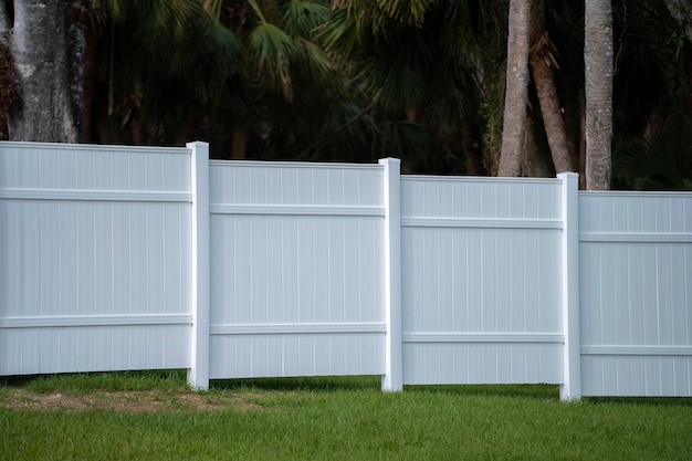 White vinyl picket fence on green lawn surrounding property grounds for backyard protection and privacy