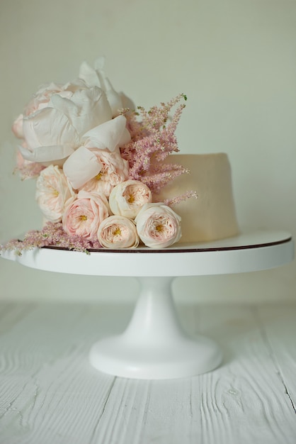 White wedding cake decorated with fresh roses, peonies and greenery