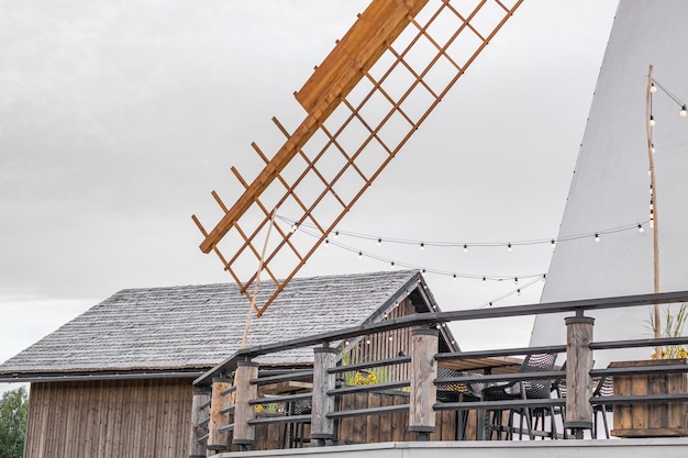 A white windmill with a wooden wing surrounded by a wooden fence Cloudy gray sky in the background